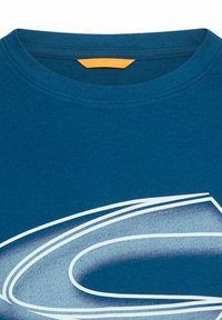 Blå bomuld T-shirt med rund hals, orange mærke og stort hvidt grafisk design med buede linjer. Glat tekstur.