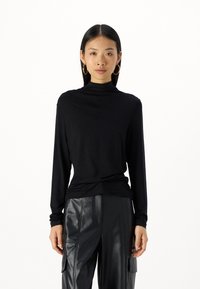Svart langermet turtleneck-genser laget av mykt stoff, har en avslappet passform med en jevn tekstur og elegant drapering. Kombinert med skinnbukser.