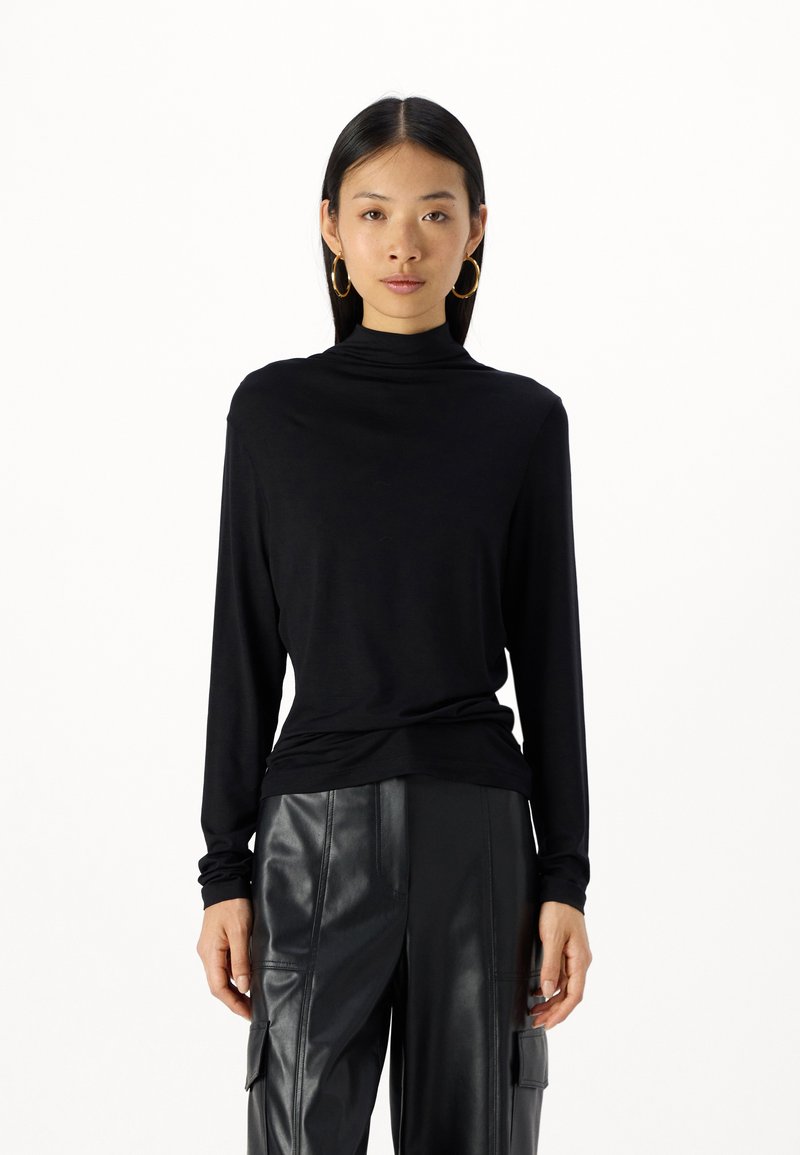 Svart langermet turtleneck-genser laget av mykt stoff, har en avslappet passform med en jevn tekstur og elegant drapering. Kombinert med skinnbukser.