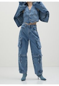 Denimoutfit som består av en kortärmad väst med knäppning och vida cargobyxor med flera fickor, i en ljusblå tvätt. Slät textur.