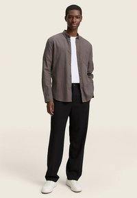 Camicia grigia leggera a maniche lunghe con bottoni e tasca, abbinata a pantaloni neri e sneakers bianche. Tessuto liscio con vestibilità comoda.