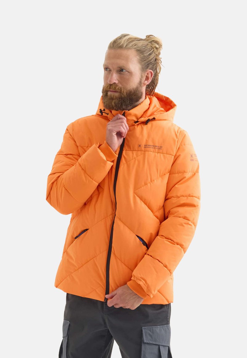 Chaqueta acolchada naranja con capucha, que presenta costuras diagonales, detalles en cremallera azul y un cierre frontal con cremallera.