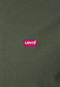 Chemise en tricot vert olive ornée d'un petit logo brodé Levi's en rose et blanc. Tissu à texture côtelée.