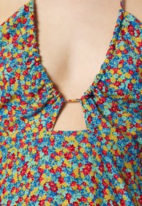 Květinové šaty s modrým, žlutým a červeným vzorem, výstřihem do V se skladáním a otvorem ve tvaru klíče na živůtku.
