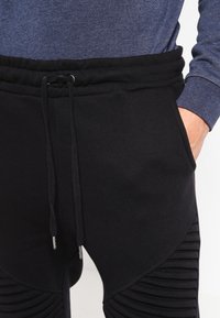 Pantalones de chándal negros con cintura ajustable, con paneles laterales acanalados texturizados y un acabado de tela suave. Con detalles en hardware plateado.