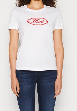 Biała koszulka z krótkim rękawem z czerwonym logo "Diesel" w owalu na piersi, noszona z ciemnoniebieskimi dżinsami.