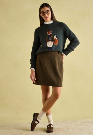 Dunkelgrüner Pullover mit Fuchs-Motiv, brauner Wollrock, cremefarbene Socken mit Punkten und braune Schuhe; hat gerippte Bündchen und ein strukturiertes Muster.