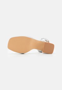 Silver high-heeled shoe with a textured upper, square toe, and a tan rubber sole featuring grooves for traction.