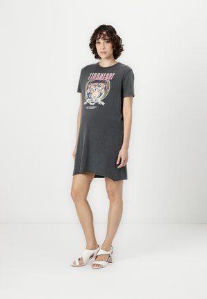 Graues T-Shirt-Kleid mit rundem Ausschnitt und kurzen Ärmeln, versehen mit einem bunten Tiger-Motiv. Kombiniert mit weißen, Riemchen-Wedge-Sandalen.