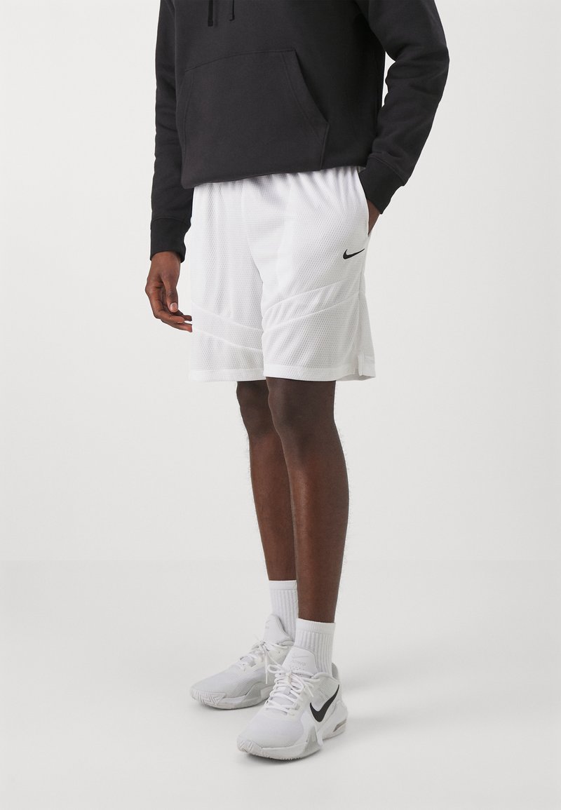 Hvide net athletic shorts med sideløbende paneler og et sort Nike-logo, parret med hvide sportsko og sokker, samt en sort hoodie.