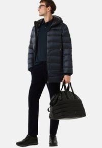 Marineblå dunjakke med hætte, lynlåslommer og ribbede manchetter. Parret med en marineblå polo, mørke bukser og en sort duffelbag.