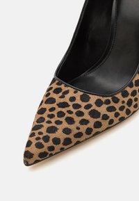 Escarpin à imprimé léopard avec un bout pointu, fabriqué dans un matériau texturé beige avec des taches noires, présentant un intérieur noir lisse.