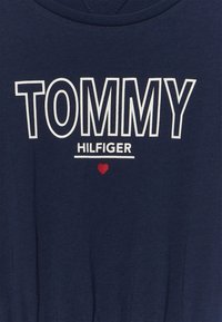 Granatowa bawełniana koszulka z napisem "TOMMY" dużymi białymi literami, a poniżej mniejszymi literami "HILFIGER" oraz małym czerwonym serduszkiem.