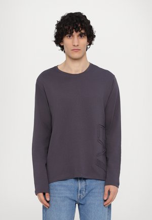 Langærmet T-shirt med rund hals i mørkegrå bomuld. Har et struktureret, præget design på venstre side. Matchet med lyseblå denimjeans.
