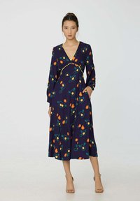 Robe florale bleu marine avec des manches longues, un décolleté en V et des motifs floraux colorés en orange et vert. Elle a une taille cintrée et une jupe fluide.