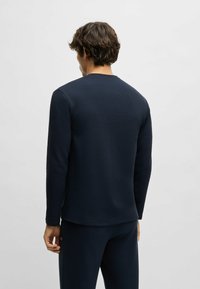 Donkerblauwe lange mouwen shirt van een textuurstof, met een ronde hals en een rechte zoom. Draagt met bijpassende donkerblauwe broek, toont de achterkant.