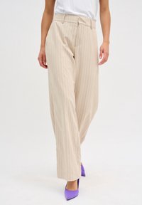 Beige pruhované kalhoty s vysokým pasem, širokými nohavicemi a předními kapsami, doplněné fialovými střevíčky s špičatou špičkou. Hladká textilie.