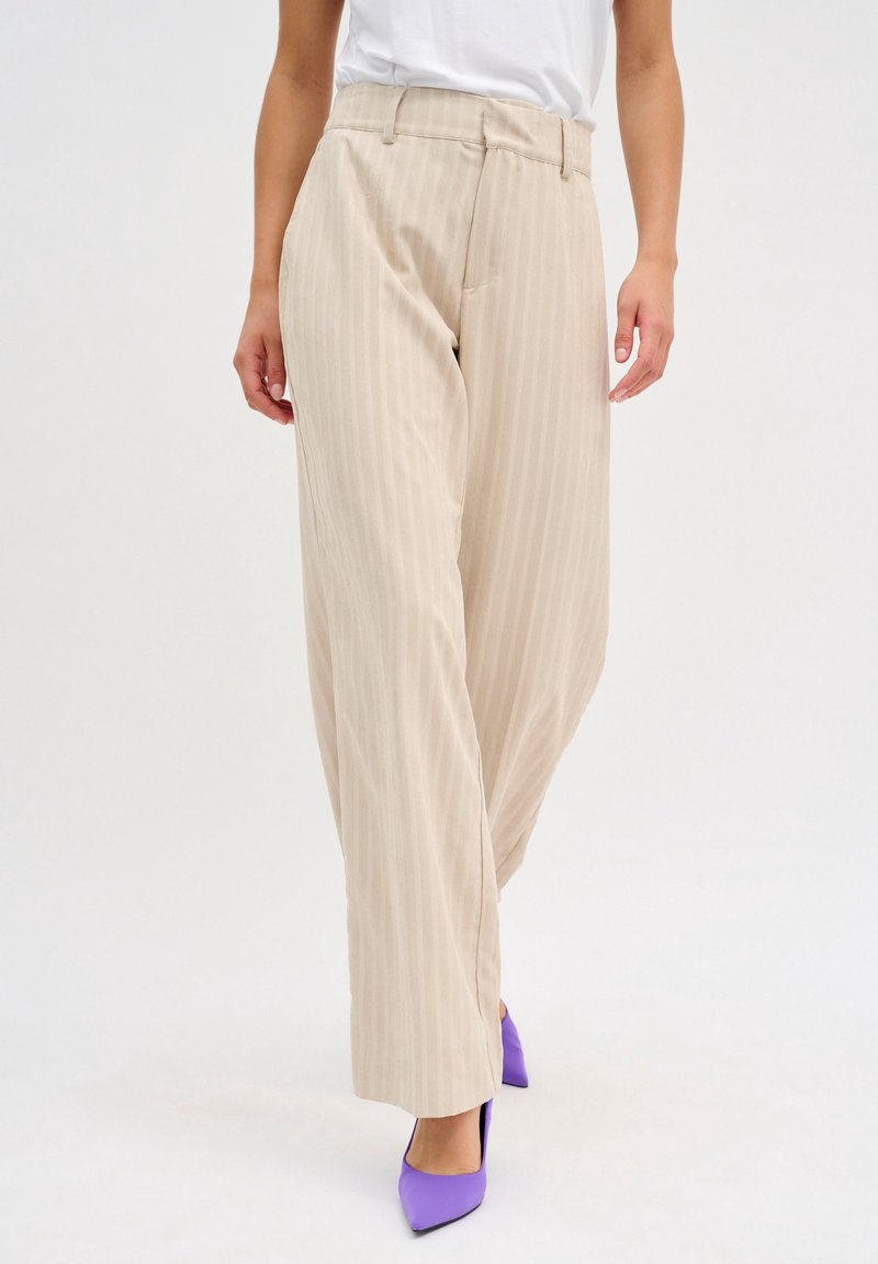 Beige pruhované kalhoty s vysokým pasem, širokými nohavicemi a předními kapsami, doplněné fialovými střevíčky s špičatou špičkou. Hladká textilie.