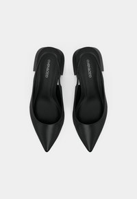 Des chaussures slingback noires à bout pointu avec une texture lisse et un design minimaliste. Elles possèdent un petit talon et des côtés découpés pour une meilleure respirabilité.
