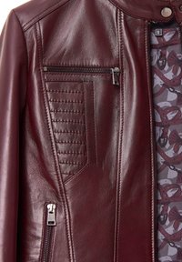 Giubbotto in pelle borgogna con tasca con zip, dettagli trapuntati e fodera decorata con design di imbracature e fiocchi.