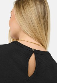 Černý top s kulatým výstřihem a otvorem na zádech, který je zajištěn malým knoflíkem. Měkká textura s jemným detailem šití.