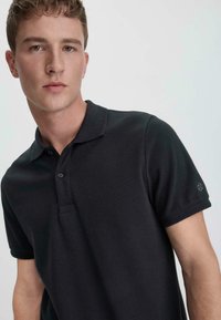Dark gray polo shirt with short sleeves, classic collar, and two buttons. Features subtle texture and a logo on the left sleeve.
