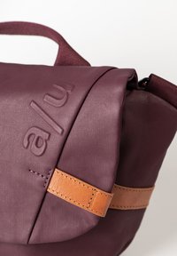 Borsa bordeaux con finitura testurizzata, dotata di tracolla in pelle e dettaglio del logo impresso. Design compatto con chiusura a patta.