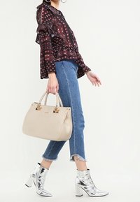 Blusa nera a fantasia con volant, jeans cropped blu chiaro, stivaletti metallici argentati alla caviglia e borsa beige con manici intrecciati.