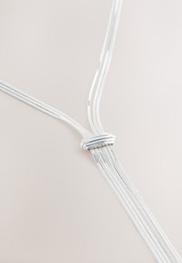 Silberne Halskette mit mehreren Strängen, bestehend aus eleganten, ineinander verschlungenen Metallsträngen, die in der Mitte, mit glatter Oberfläche und reflektierender Textur, geknotet sind.