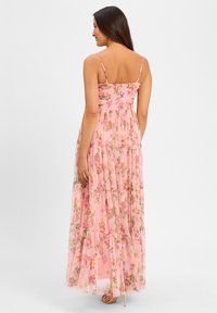 Maxi dress in sheer pink fabric with floral print. Spaghetti straps, smocked bodice, tiered skirt, and a flowing design.
