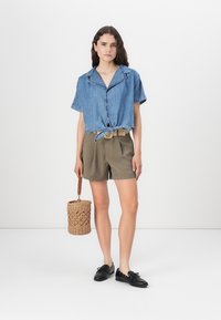 Denim skjorta med korta ärmar, knuten i midjan, kombinerad med olivgröna shorts. Accessoarer med en rund flätad handväska.