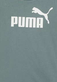 Zelena bombažna majica s širokim belim logotipom "PUMA" in grafiko skačeče pumaste, okrogel elastičen ovratnik in kratkimi rokavi.