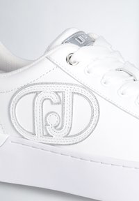 Sneaker bianco con tomaia in pelle testurizzata, lacci in poliestere e un accento di logo ricamato in argento. Suola in gomma liscia.