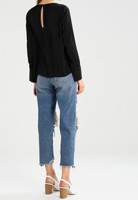 Mustassa pitkähihaisessa puserossa on avara takakappale, joka on yhdistetty vaalenvärisiin, kulutettuihin korkeavyötäröisiin farkkuihin sekä valkoisiin paksupohjaisiin sandaaleihin.