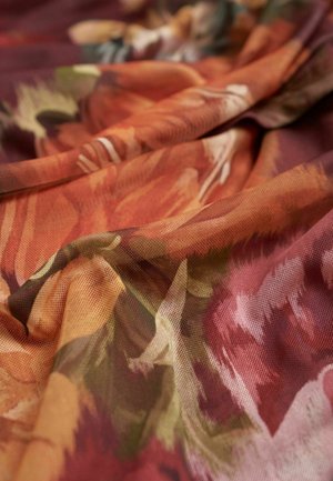 Strukturiertes Gewebe mit floralem Muster in warmen Farbtönen von Orange, Rot und Grün, drapiert, um sein fließendes Design zu präsentieren.