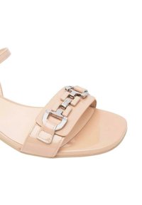 Sandal in pelle verniciata beige con una fascia larga, dettagli in metallo argentato e una punta quadrata piatta. Texture liscia e stile minimalista.