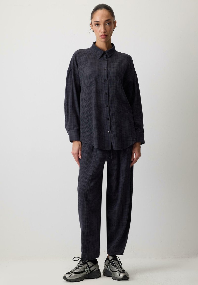 Dark plaid button-up shirt with a collar, paired with loose-fitting plaid trousers. Made of soft fabric, features a relaxed silhouette. Gray sneakers.