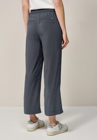 Grijze, ruime broek met een elastische tailleband en twee achterzakken. Afgewerkte zoom bij de enkel, gecombineerd met witte sneakers.