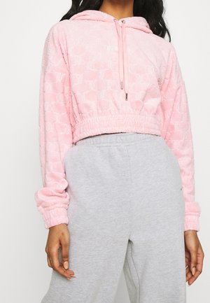 Personne portant un sweat à capuche court rose clair avec un motif texturé et un pantalon de survêtement gris taille haute avec taille élastique.