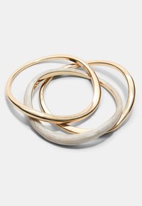 Set di tre bracciali; due in metallo dorato con una finitura lucida, uno con una superficie bianca testurizzata. Tutti presentano forme circolari intrecciate.