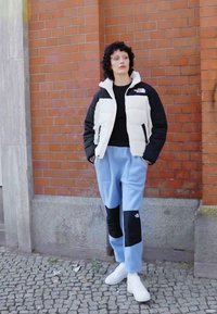 Čierna a biela nafukovacia bunda s vysokým golierom, ktorá je skombinovaná so svetlomodrými teplákovými nohavicami s čiernymi záplatami. K outfitu sa hodia biele tenisky.
