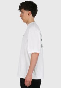 T-shirt en coton blanc à manches courtes, col rond, avec du texte imprimé à l'avant et à l'arrière. Coupe décontractée, texture douce.