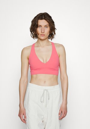 Top desportivo rosa suave com decote profundo e alças largas, combinado com calças largas, de cor clara, cropped, com cintura elástica ajustável.