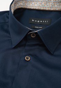 Marineblaue Kragenshirt mit einem gemusterten Innenkragen, braunen Knöpfen und einem "bugatti easy care"-Label für Komfort und Pflege.