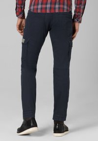 Navy cargo pants made of cotton, featuring side pockets, tapered legs, and elastic cuffs, paired with black shoes and a red checkered shirt.