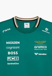 Grøn bomulds t-shirt med rund halsudskæring, med en krave i sort og brune striber. Viser flere hvide og guld logoer.