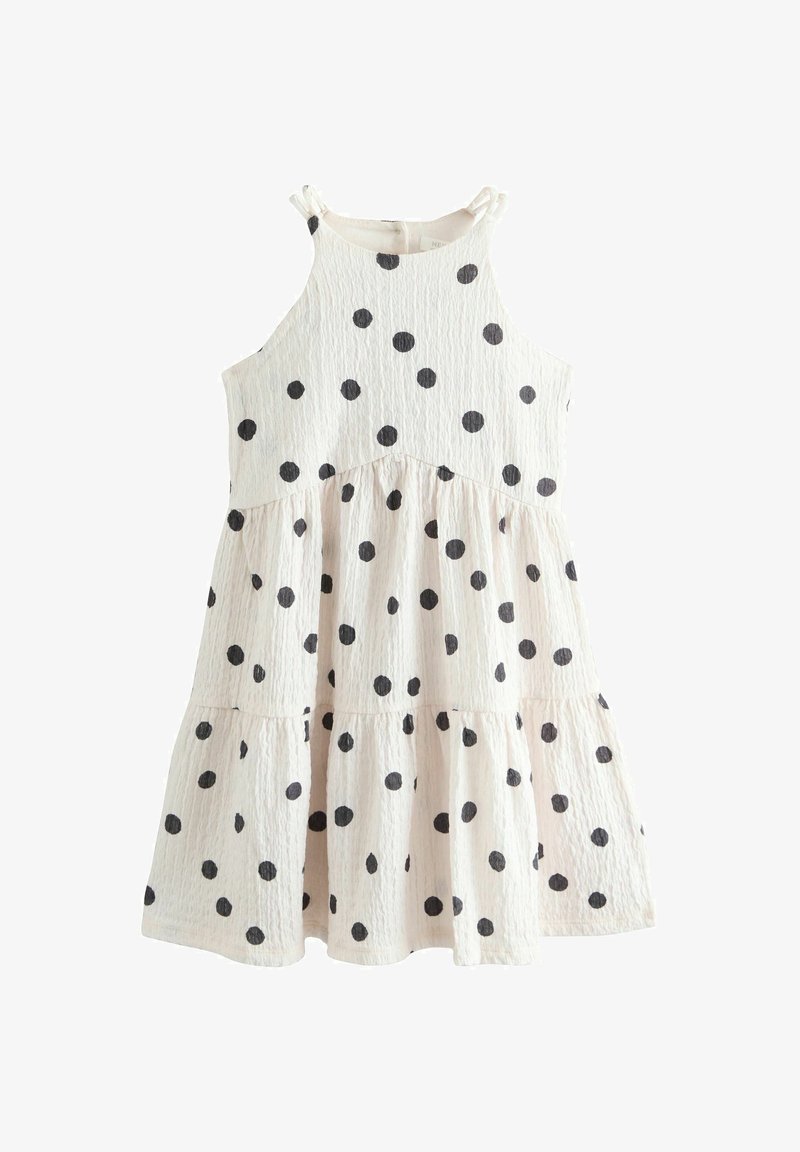 Robe d'été blanche sans manches à pois noirs, avec jupe à volants et fines bretelles nouées en nœuds.