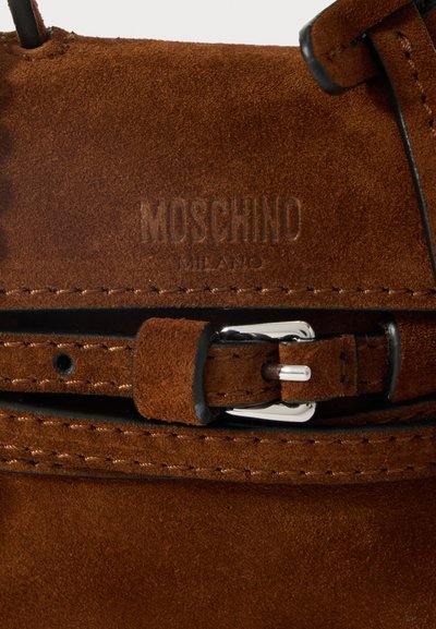 Ruda zomša medžiaga su įspaudytu MOSCHINO MILANO logotipu ir atitinkančia zomšos juosta su sidabriniu sagtimi ir juodu kraštu.