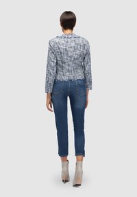 Veste cropped tissée bleue avec une finition texturée, associée à un jean en denim foncé et des bottines gris clair à talons hauts.