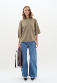 Khaki színű, oversized pulóver széles ujjakkal, világoskék, magas derekú farmernadrággal párosítva. Sötétbarna bőr táskát tart, és fekete hegyes orrú lapos cipőt visel.